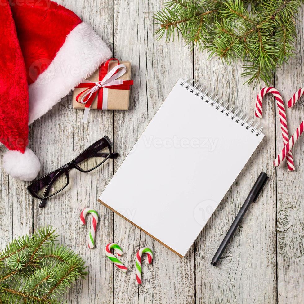 Christmas and Business Items with Copy Space cropped Santa Cap Notepad Pen Glasses and decorated Gift Box and fir tree photo