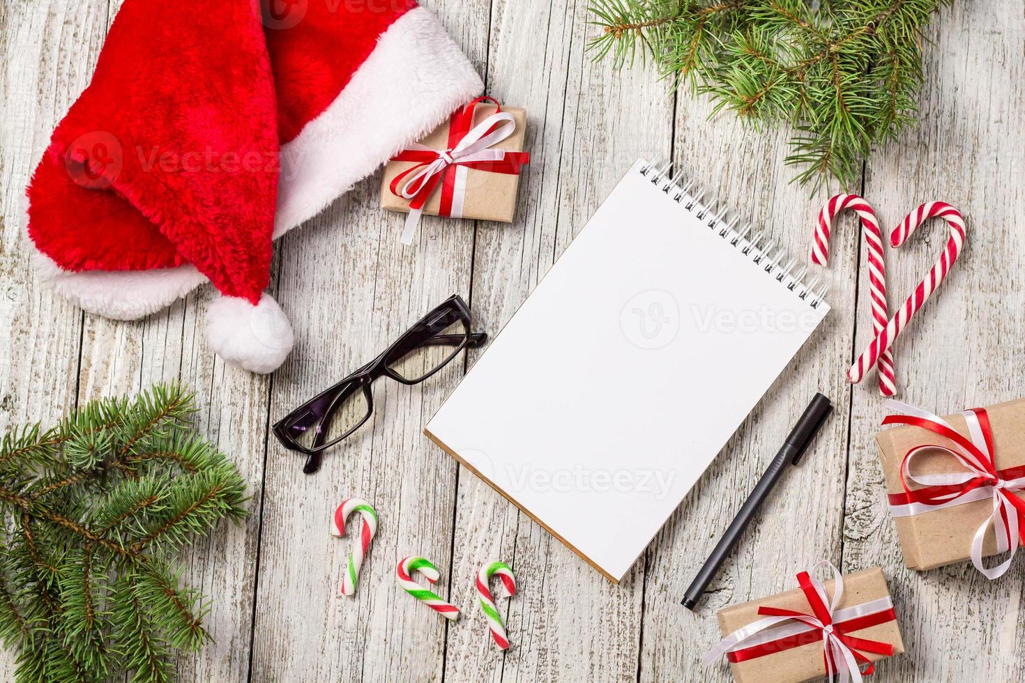 Christmas and Business Items with Copy Space cropped Santa Cap Notepad Pen Glasses and decorated Gift Box and fir tree photo
