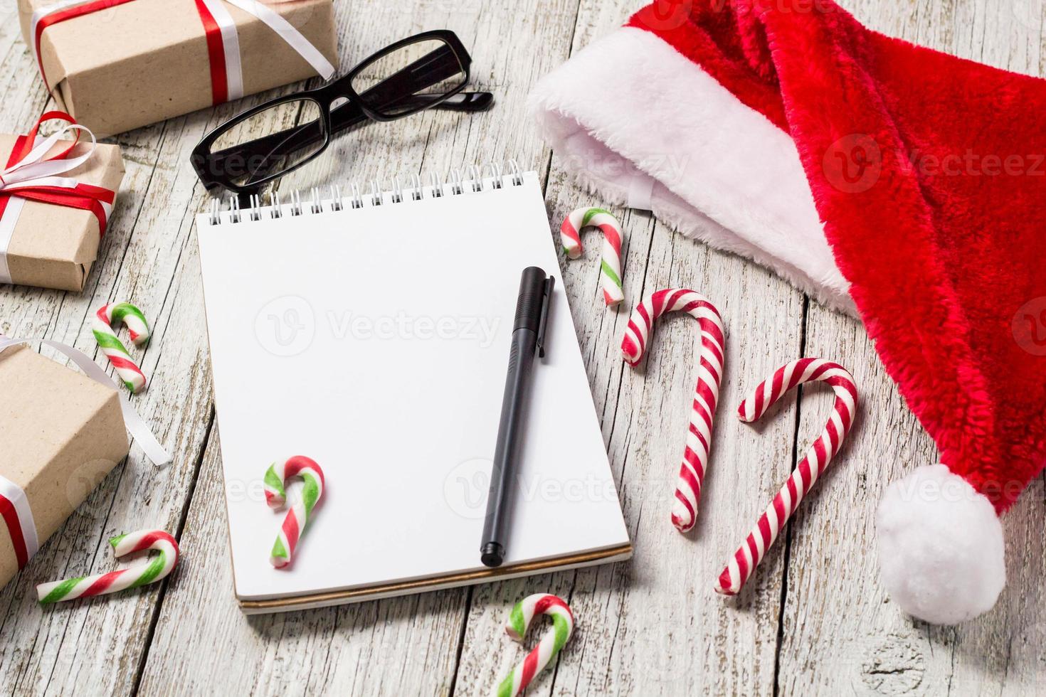 Christmas and New Year Items with Copy Space Santa Cap Notepad Pen Glasses and decorated Gift Boxes photo