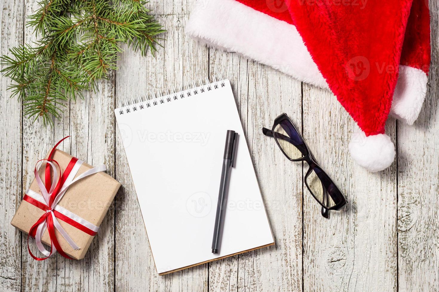 Christmas and Business Items with Copy Space cropped Santa Cap Notepad Pen Glasses and decorated Gift Box and fir tree photo