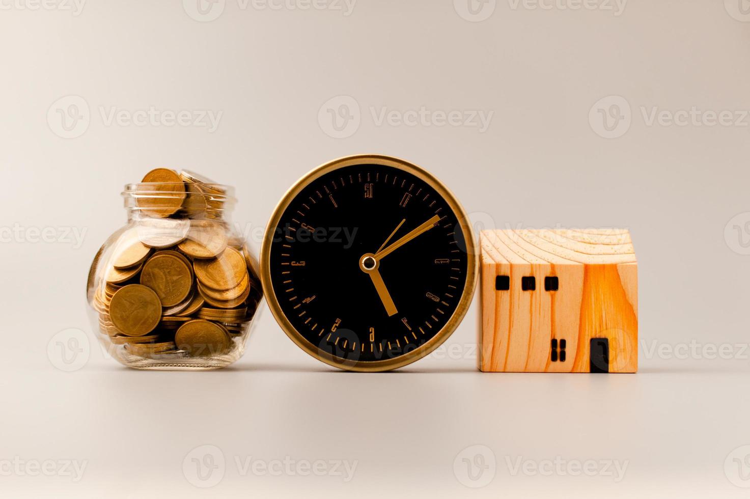 Golden alarm clock, model wooden house and silver gray background, coin saving ideas to build a home and personal business for a sustainable future. photo