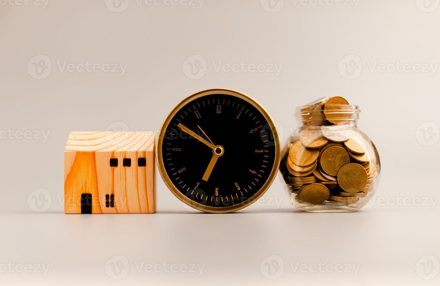 Golden alarm clock, model wooden house and silver gray background, coin saving ideas to build a home and personal business for a sustainable future. photo