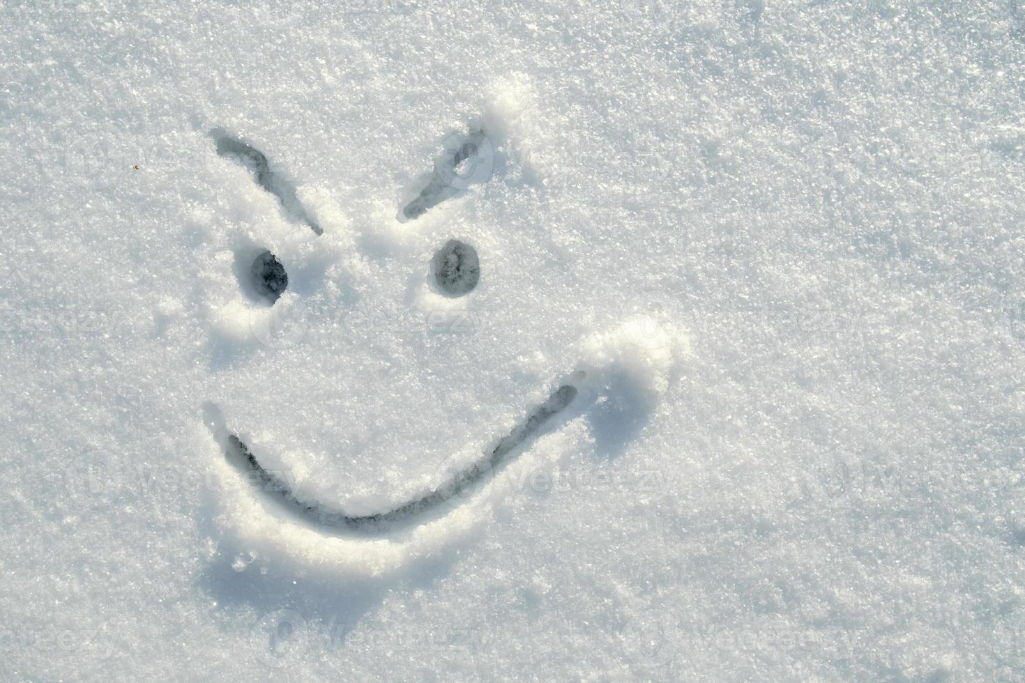 Face of an insidious, angry, smiley, painted on the snow on a sunny winter day. Copy space. Top view. photo