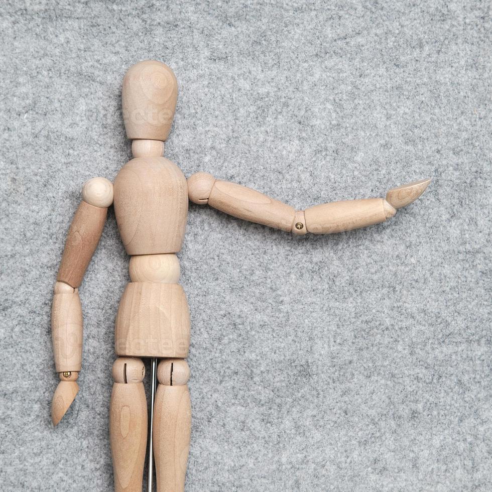 Small wooden figurine stretches out its hand and points to something against a gray felt background. Copy space. Top view. photo