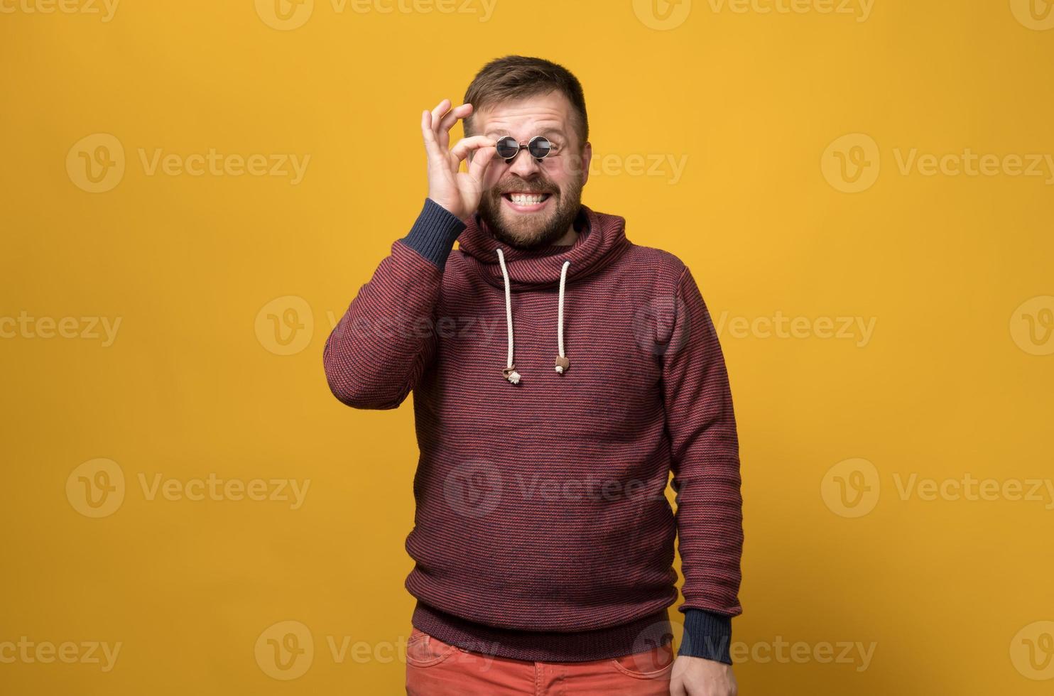 Cheerful Caucasian bearded man holds toy sunglasses like pince-nez to his eyes, with a bizarre grimace and grin. Yellow background. photo