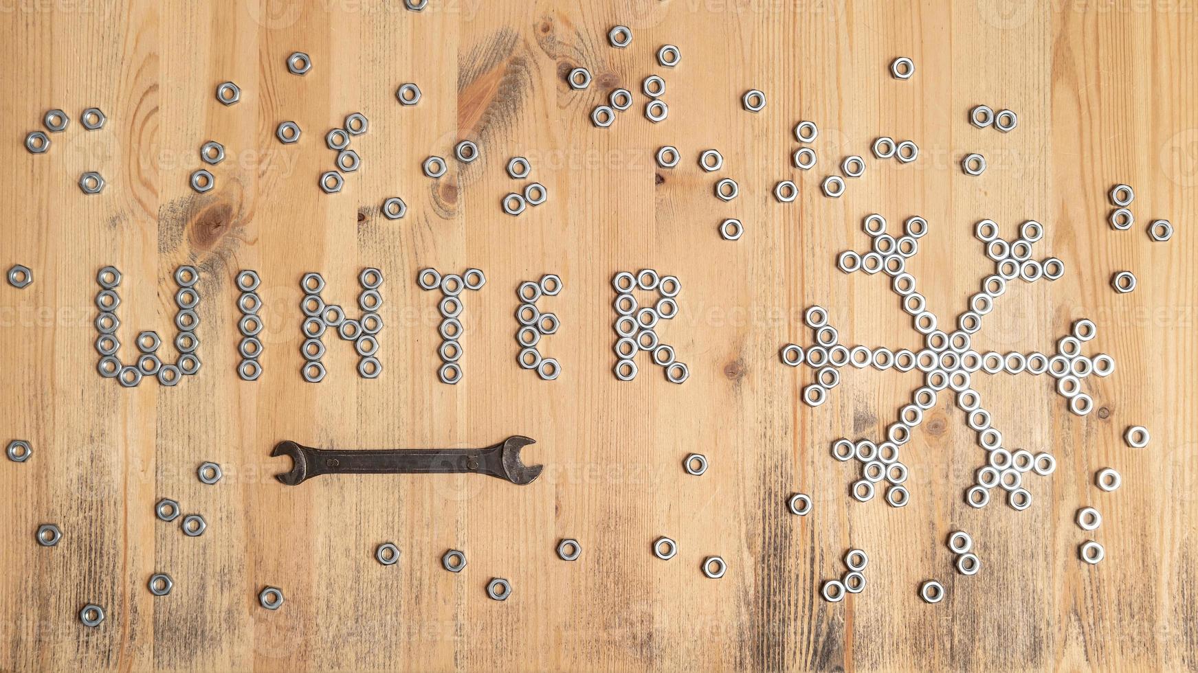Word winter and a snowflake are lined with metal nuts on table, next to a wrench. New Year and Christmas holiday wait concept. photo