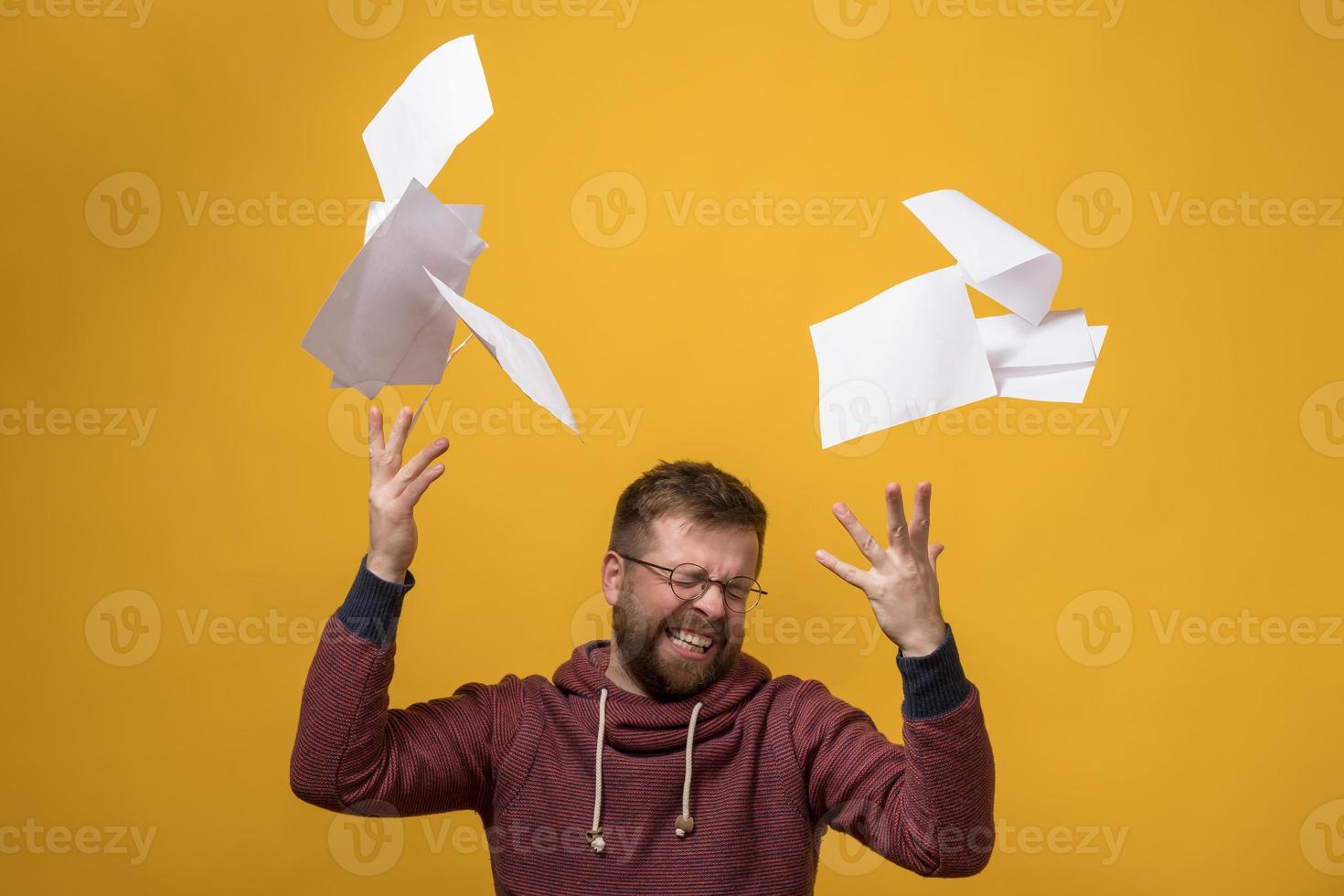 Man is stressed, he throwing a stack of white paper up, squeezes eyes shut and clenching her teeth. Bad working day. Copy space. photo