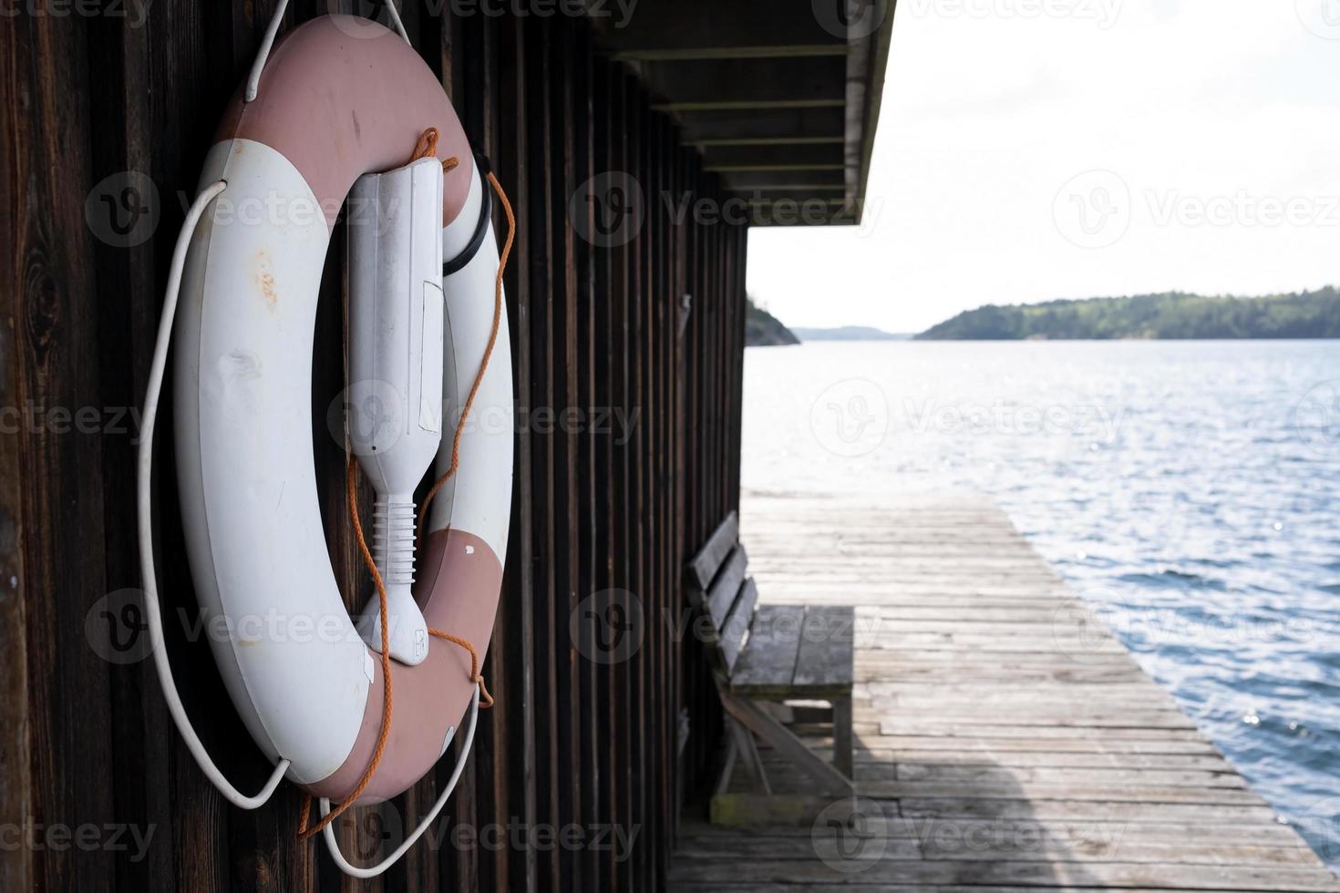 Lifebuoy hangs on an old wooden hut on the pier, against the backdrop of a beautiful landscape of the sea and rocks. Concept of a safe holiday. photo