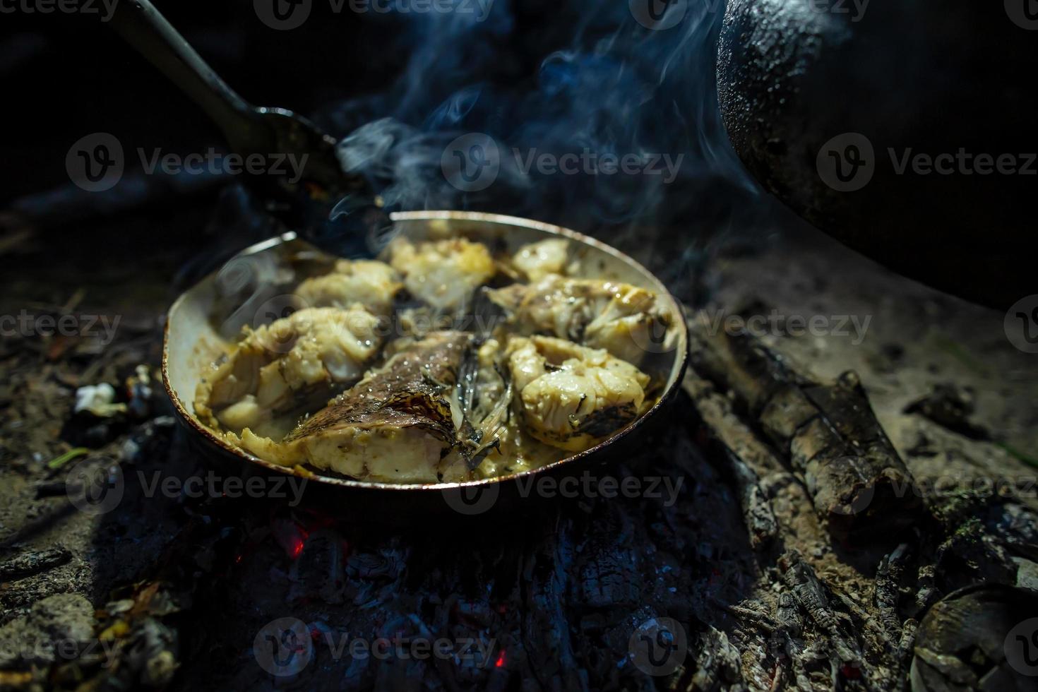 Large chunks of freshly caught fish are fried in a pan over a campfire, over coals, in the evening, at a camping. Lifestyle. photo