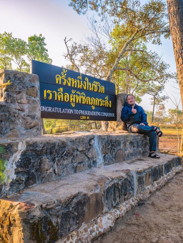 Asian traveler with Congratulation to phukradueng conquerorsign on the top of Phu Kradueng mountain national park in Loei City Thailand.Phu Kradueng national park the famous Travel destination photo