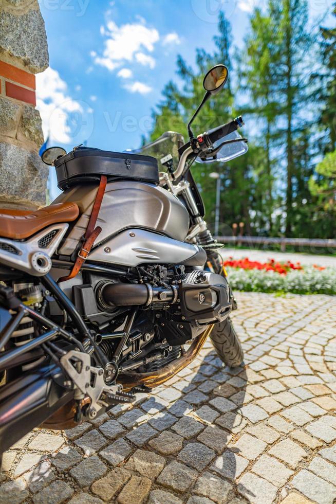 motocicleta de primer plano estacionada en la carretera de entrada con luz cálida y soleada. árboles forestales borrosos, flores de parque y camino de grava. moto vintage clásica, actividad recreativa deportiva al aire libre. viajes de naturaleza foto