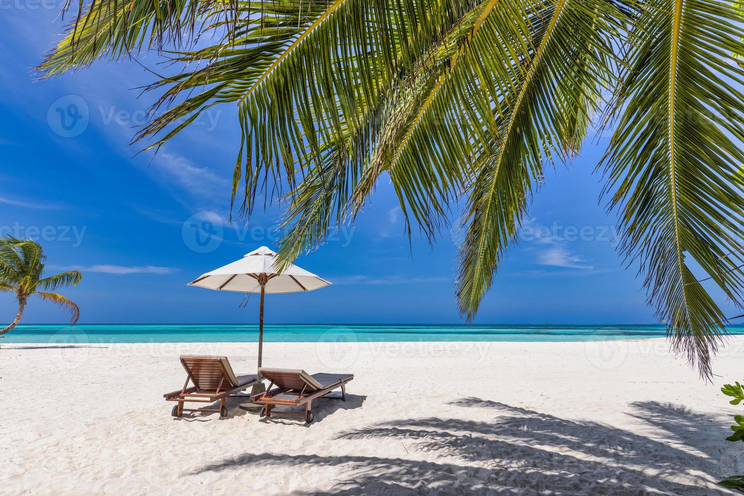 hermoso paisaje tropical, un par de sillas tumbonas sombrilla bajo hojas de palma. fondo de verano, playa de viajes exóticos, costa paradisíaca de día soleado. increíble paisaje, mar arena cielo relax resort vacaciones foto