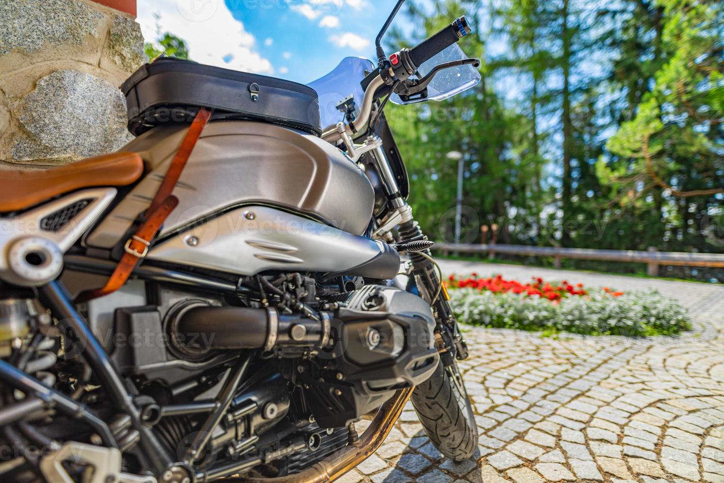 motocicleta de primer plano estacionada en la carretera de entrada con luz cálida y soleada. árboles forestales borrosos, flores de parque y camino de grava. moto vintage clásica, actividad recreativa deportiva al aire libre. viajes de naturaleza foto