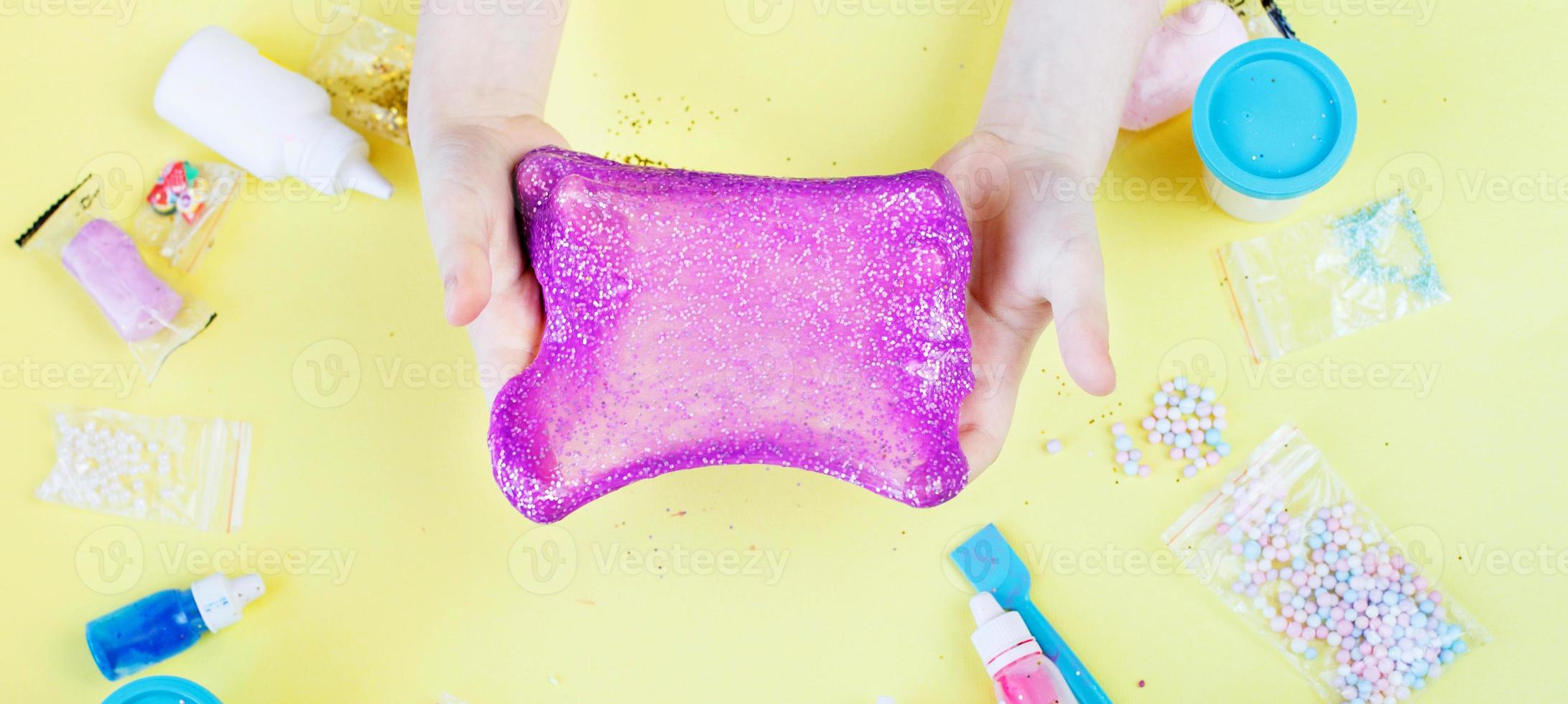 Making slime at home. child stretching colorful slime. DIY concept. hands make slime with sequins on yellow background photo