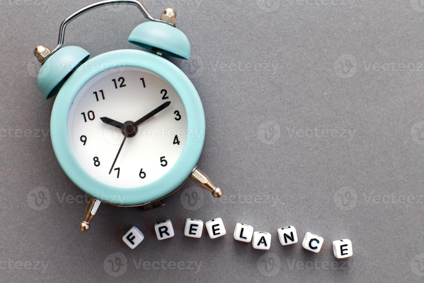 Alarm clock and word freelance made from plastic cubes of beads on gray background photo