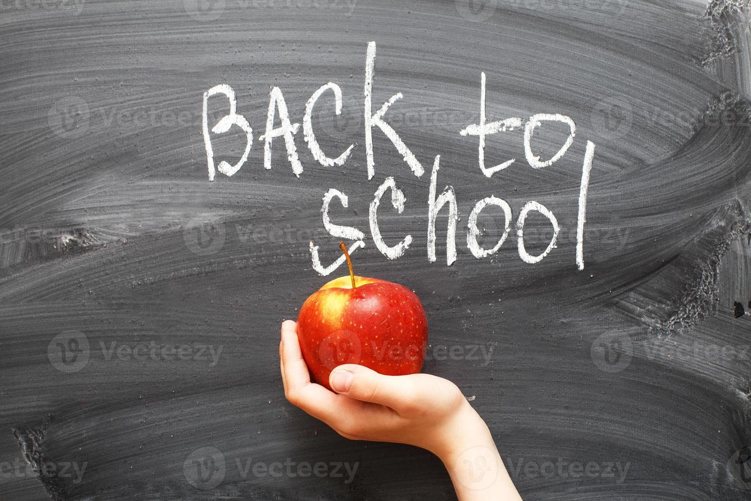 child's hand holding an apple near chalkboard. Back to school concept background photo