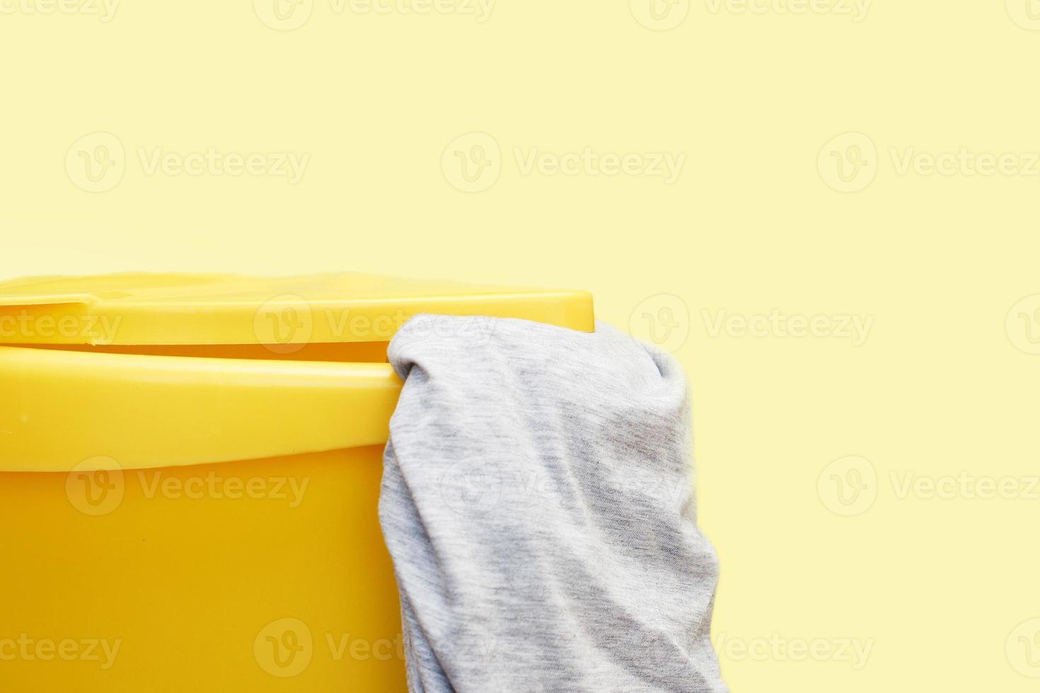 Yellow plastic laundry basket with gray clothing on yellow background photo