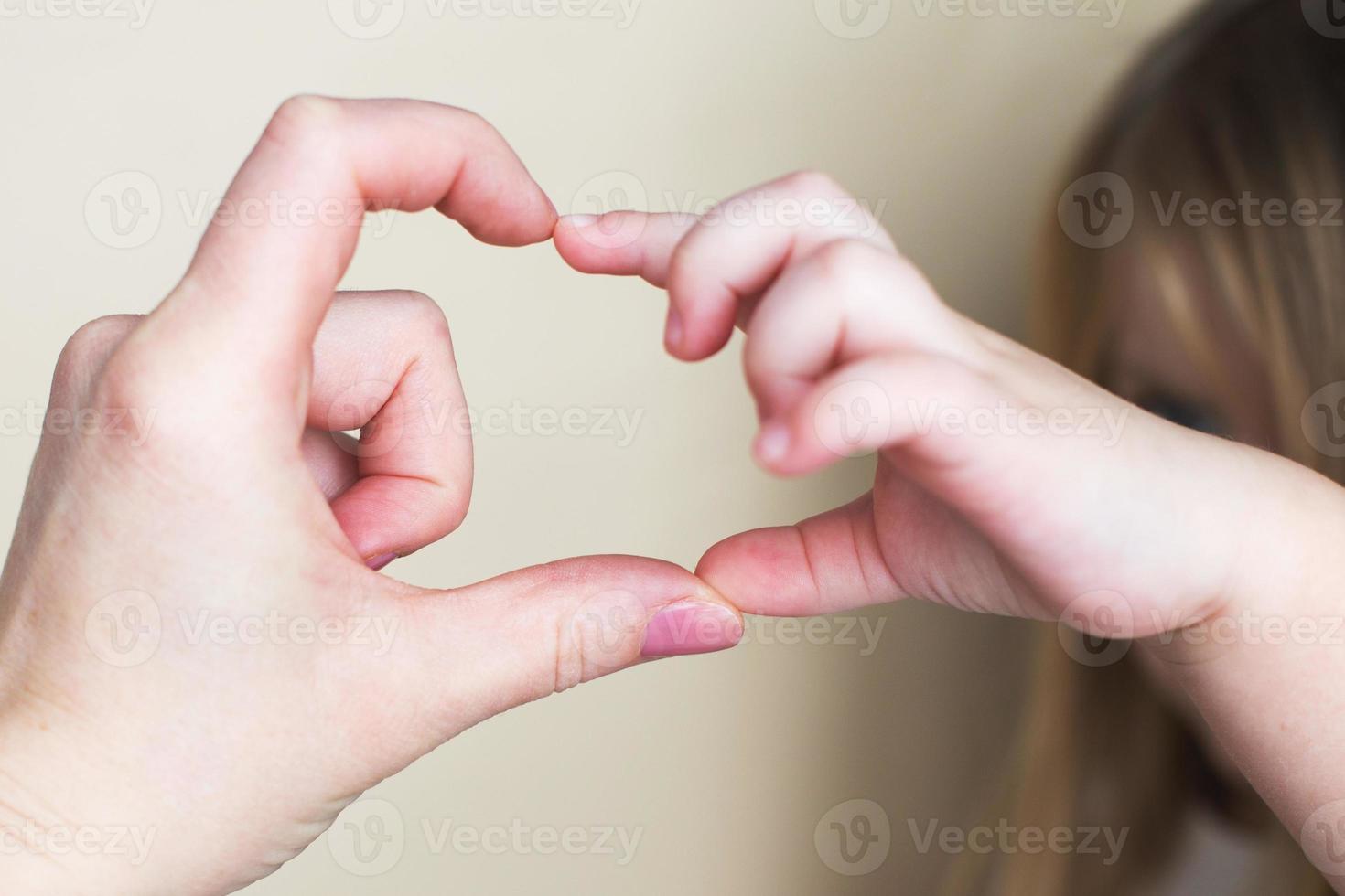 forma de corazón creada a partir de las manos de la niña y las manos de su madre sobre fondo beige. foto