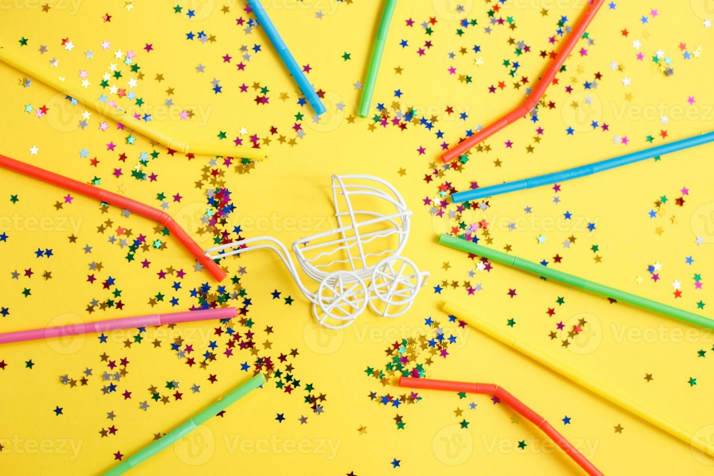 birthday party.baby stroller with stars confetti sequins and multicolored drinking straws on yellow background photo
