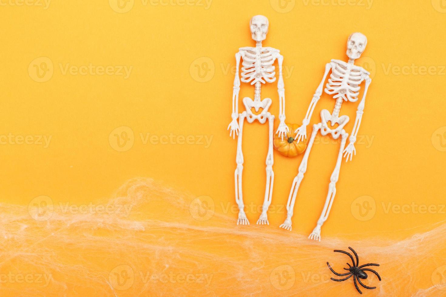 esqueletos con calabaza, telaraña y arañas negras sobre fondo naranja. concepto de halloween foto