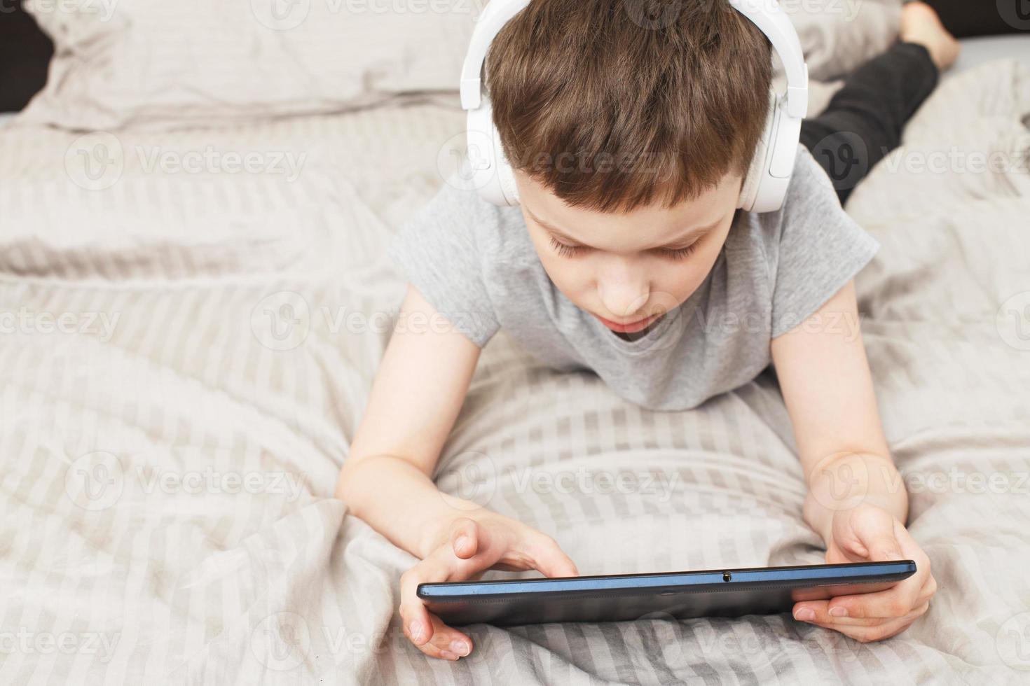 child boy lying on bed with pc tablet with wireless headphones photo
