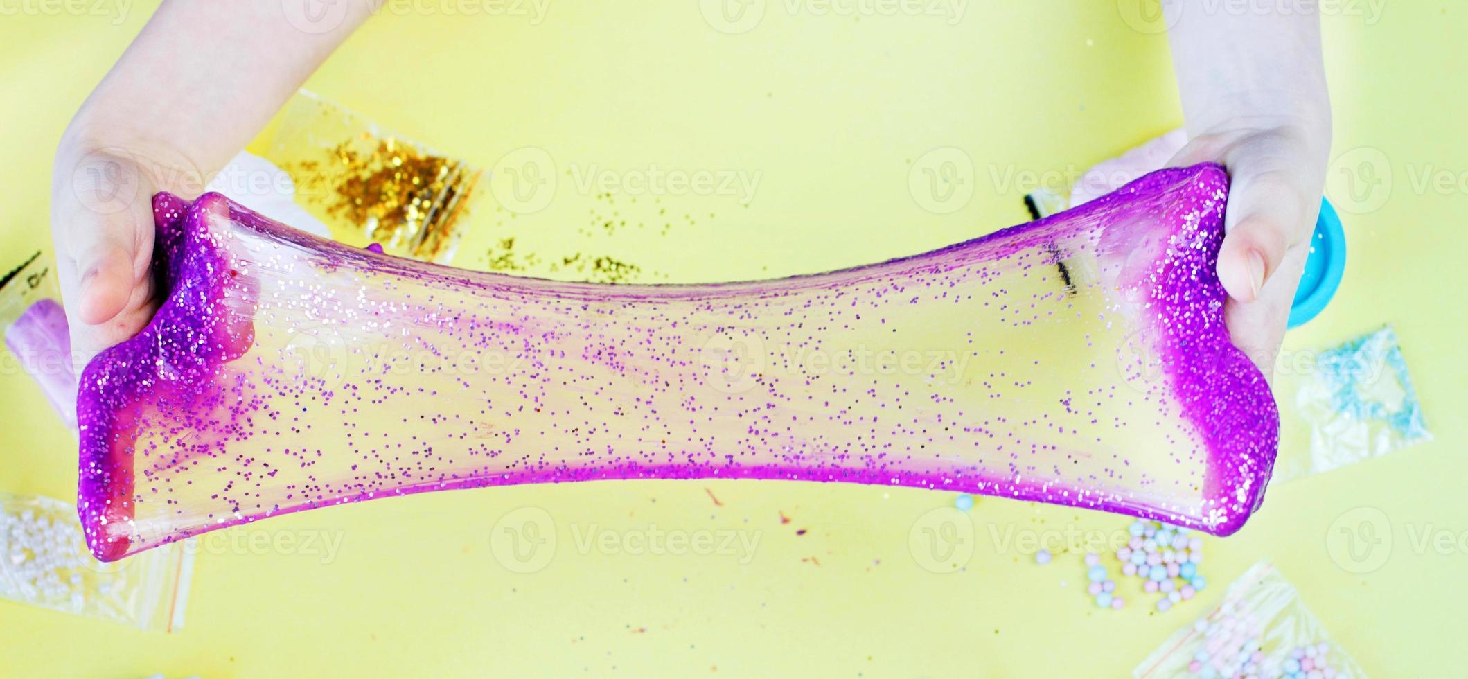 Making slime at home. child stretching colorful slime. DIY concept. hands make slime with sequins on yellow background photo