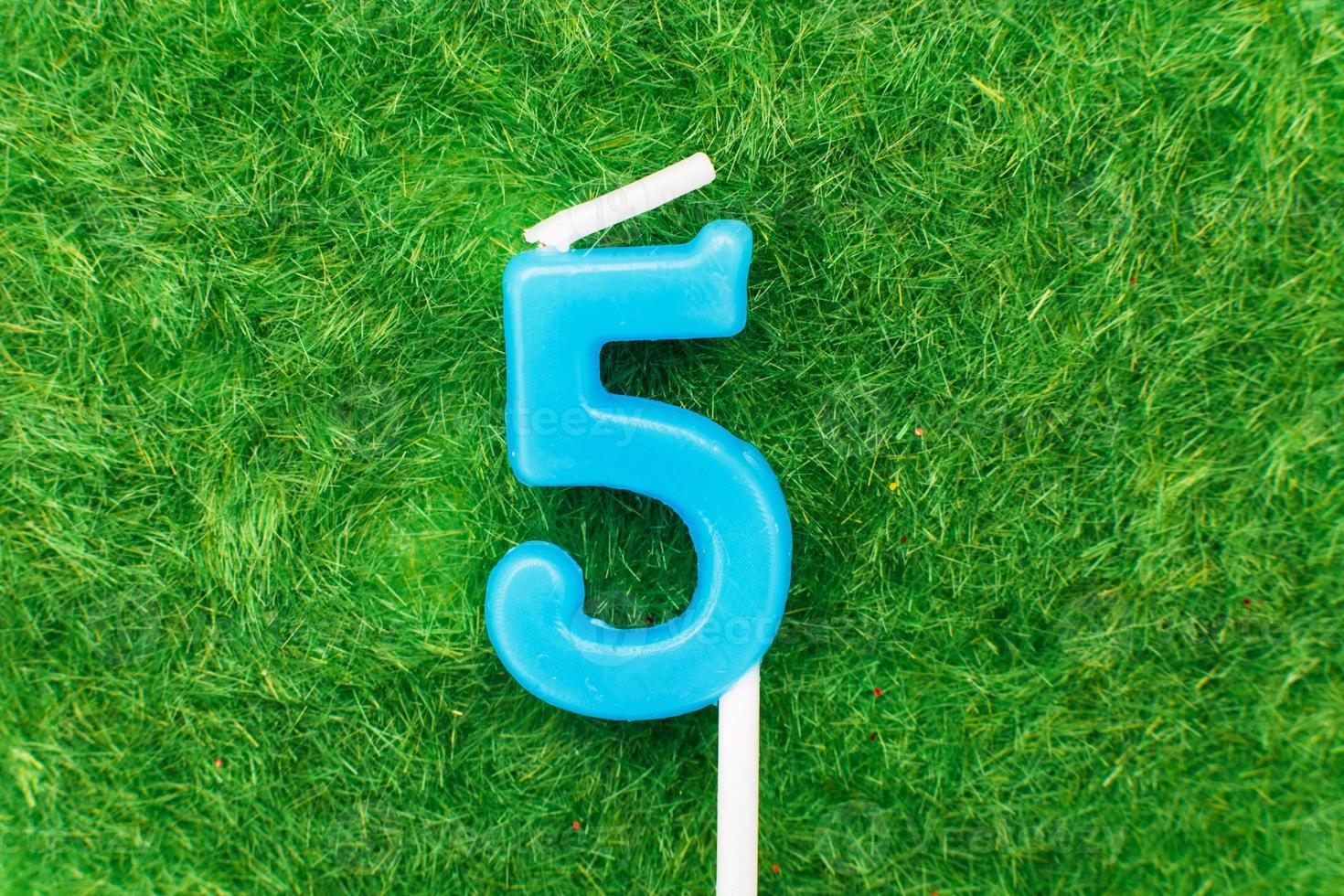 candle in the form of number 5 on the green grass background, a place for a greeting text photo