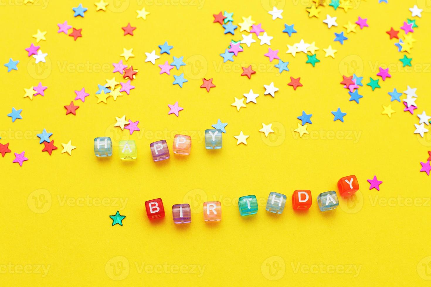 inscription happy birthday and multicolored confetti in the form of stars on yellow background photo