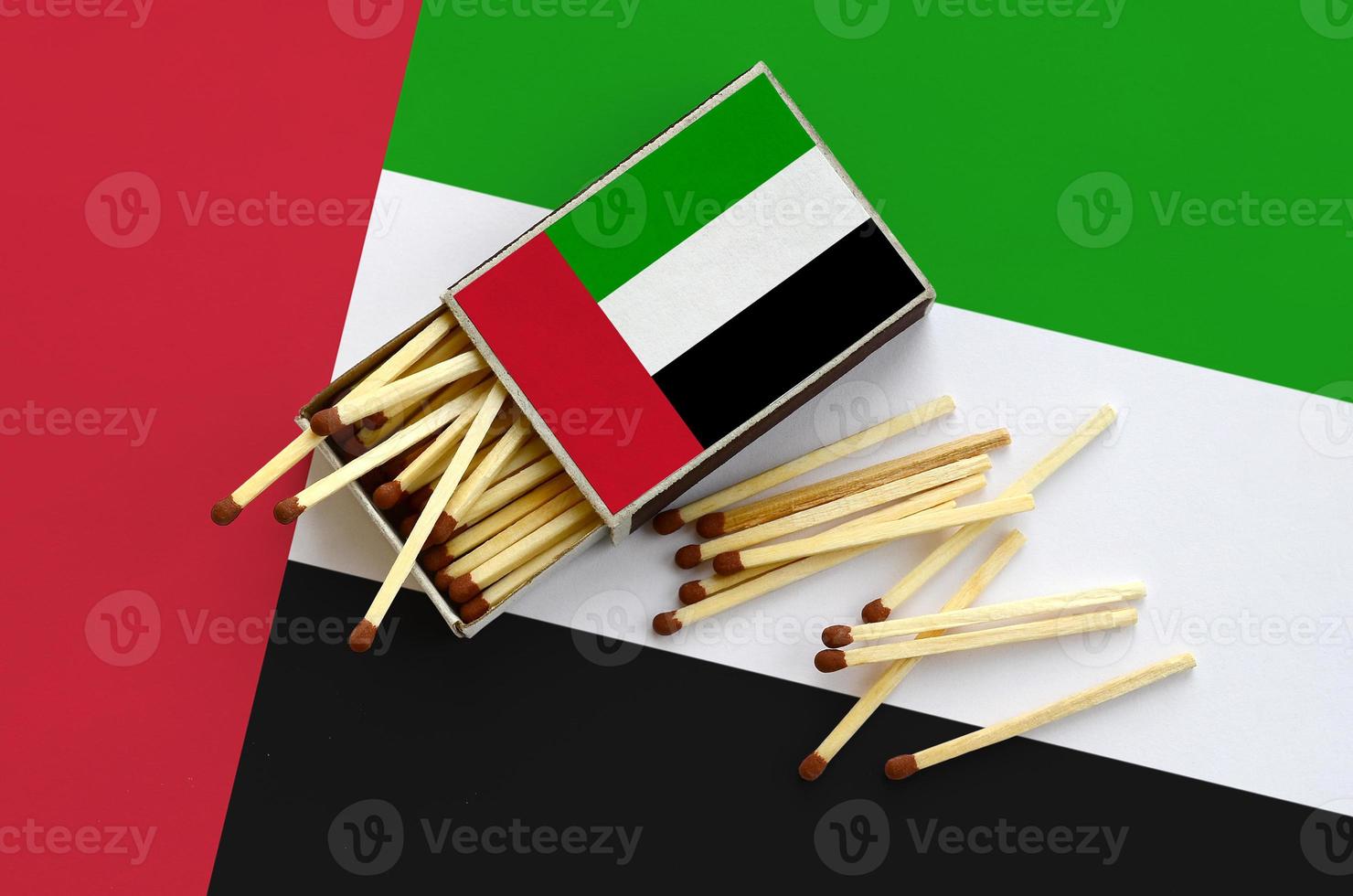 United Arab Emirates flag is shown on an open matchbox, from which several matches fall and lies on a large flag photo