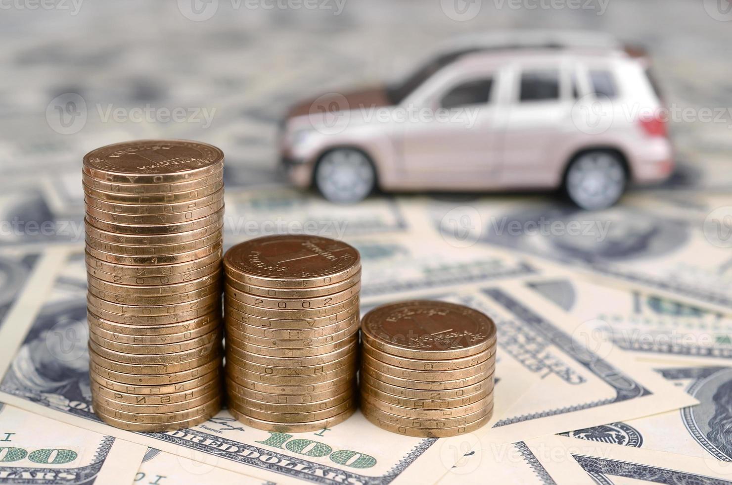 Toy car model at the stacks of golden coins lies on many dollar bills photo