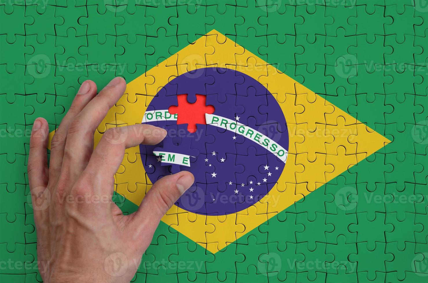 Brazil flag is depicted on a puzzle, which the man's hand completes to fold photo