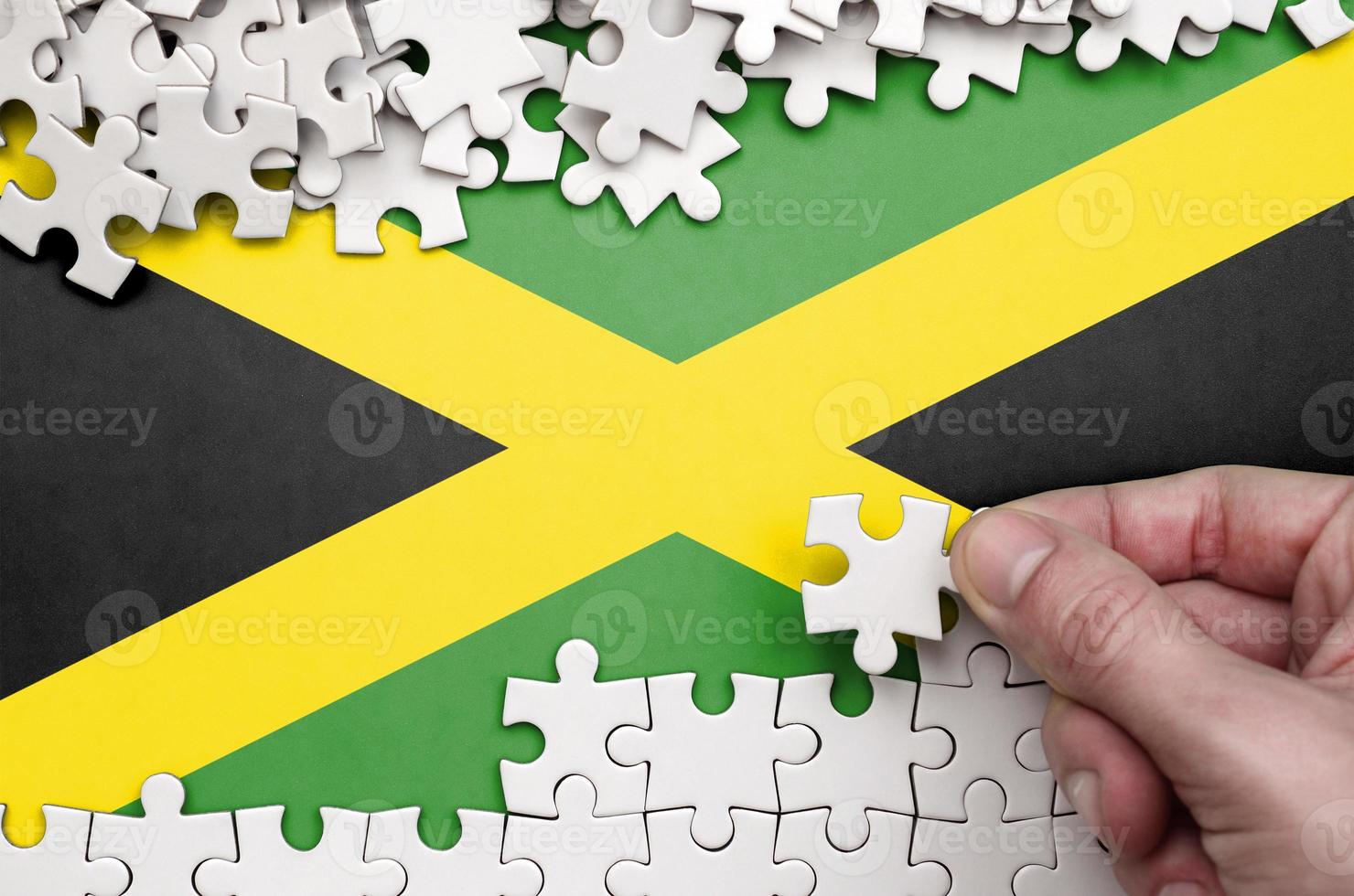 Jamaica flag is depicted on a table on which the human hand folds a puzzle of white color photo