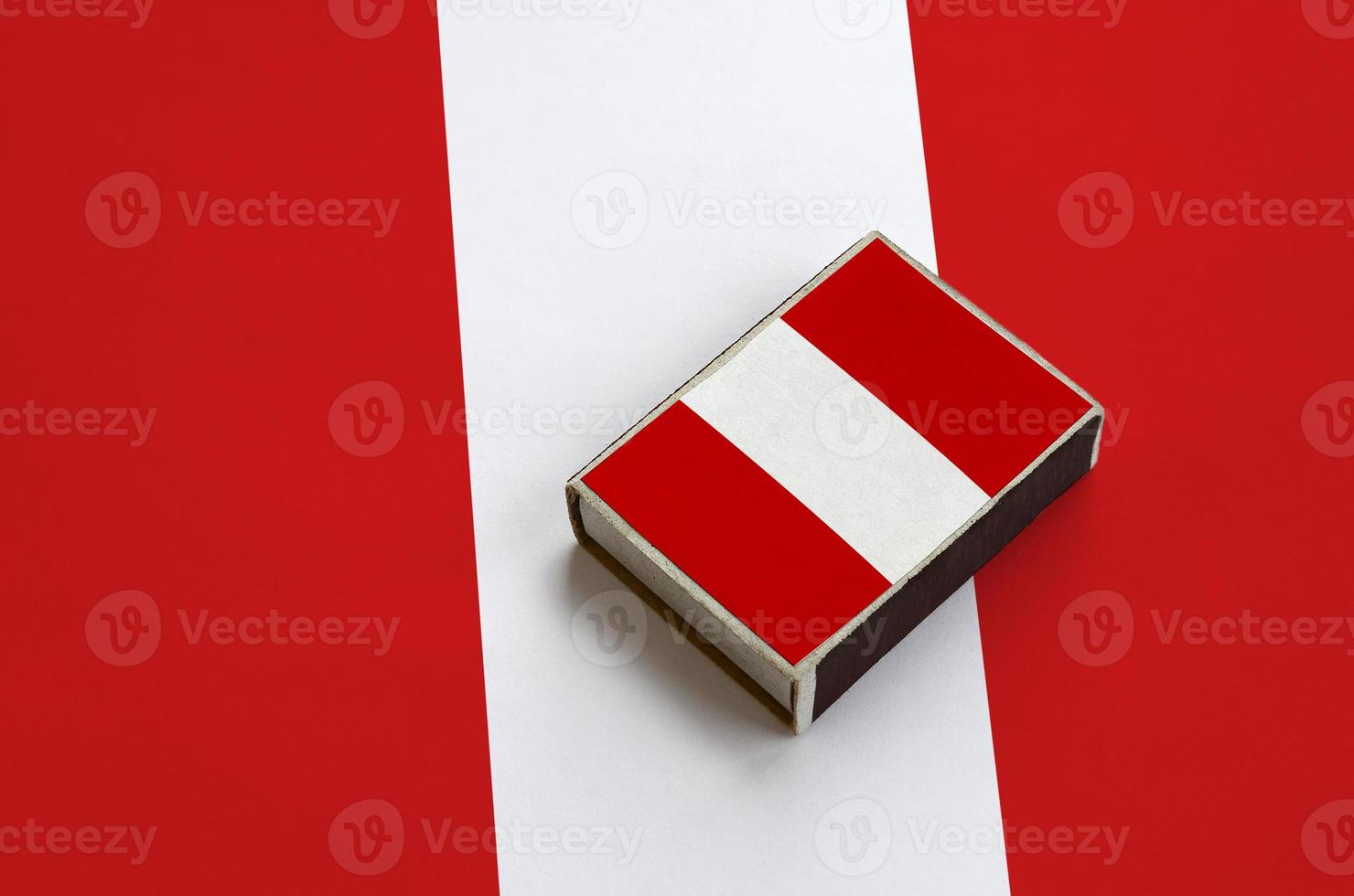 Peru flag is pictured on a matchbox that lies on a large flag photo