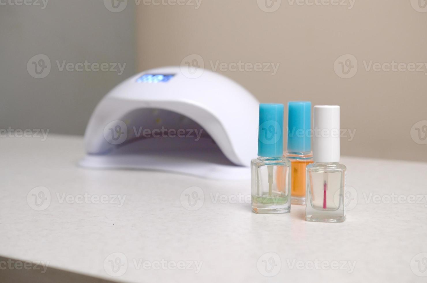 luces de lámpara de diodo uv para uñas y juego de esmalte de uñas cosmético para manicura y pedicura sobre fondo de mesa blanco foto