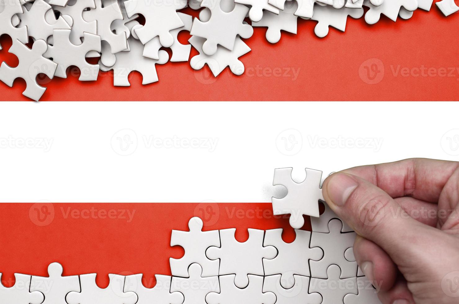 Austria flag is depicted on a table on which the human hand folds a puzzle of white color photo
