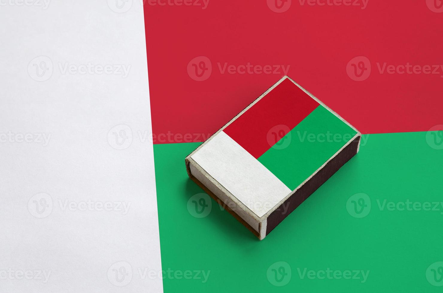 Madagascar flag is pictured on a matchbox that lies on a large flag photo