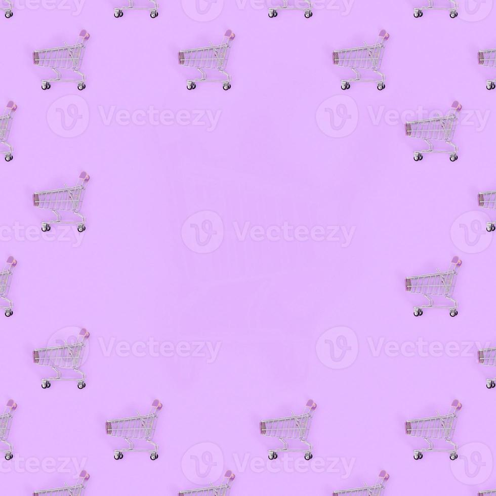 Shopping addiction, shopping lover or shopaholic concept. Many small empty shopping carts perform a pattern on a pastel colored paper background. Flat lay composition, top view photo