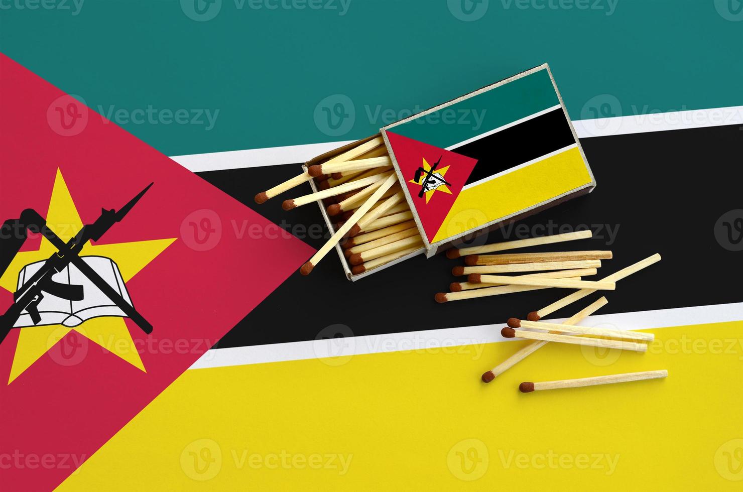 Mozambique flag is shown on an open matchbox, from which several matches fall and lies on a large flag photo