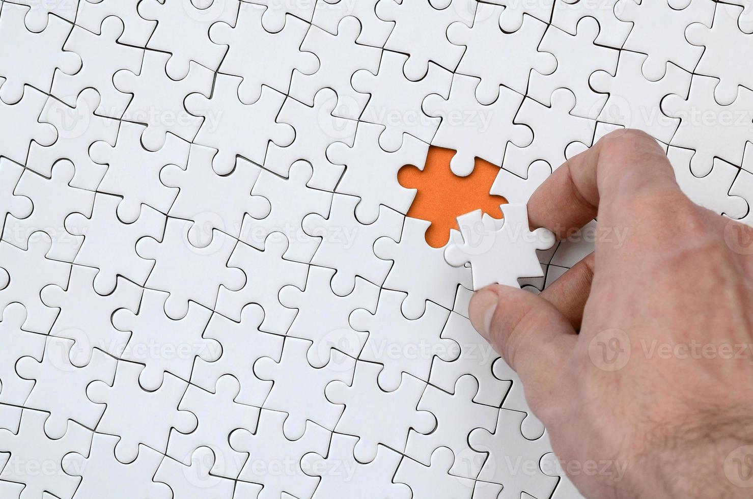 The texture of a white jigsaw puzzle in the assembled state with one missing element that the male hand puts in photo