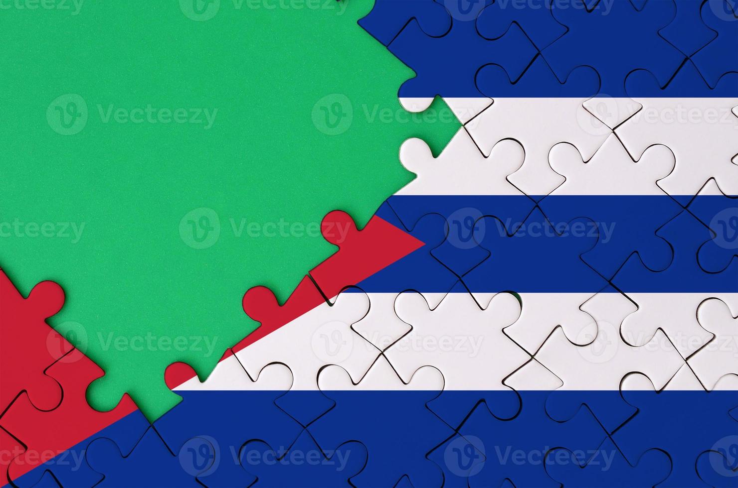 Cuba flag is depicted on a completed jigsaw puzzle with free green copy space on the left side photo