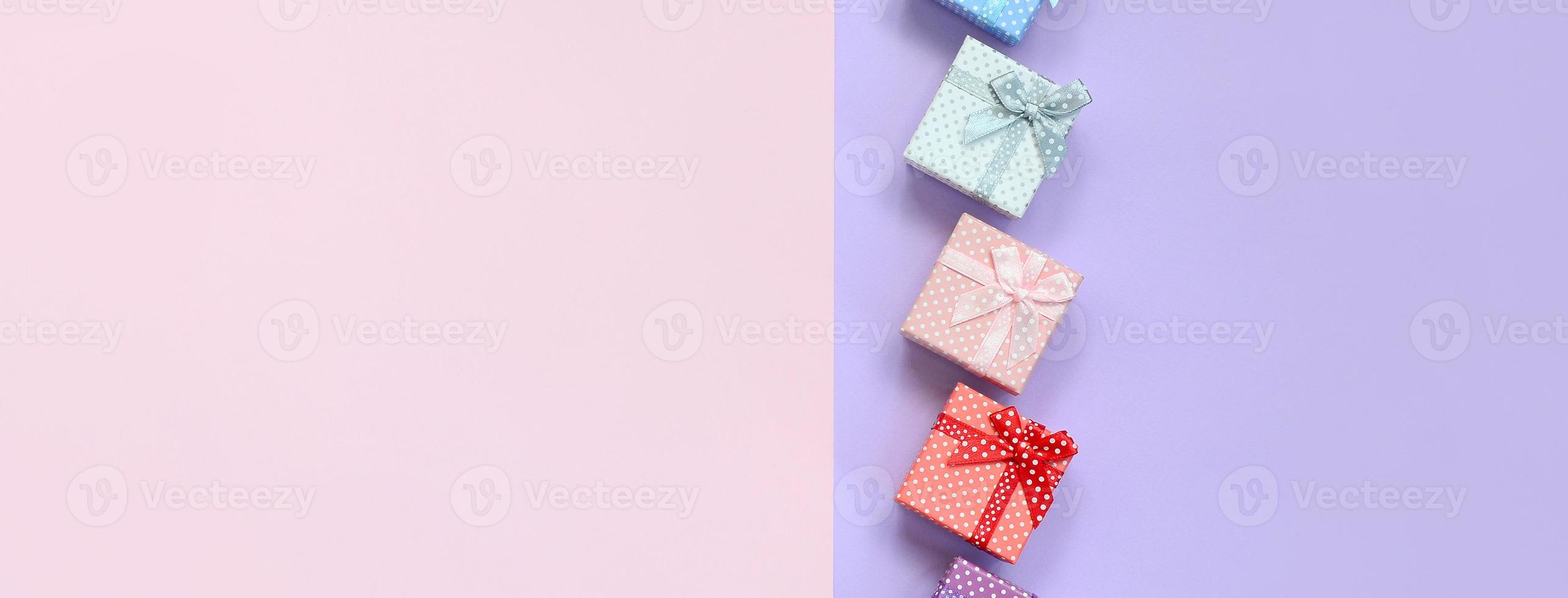 Small gift boxes of different colors with ribbons lies on a violet and pink color background photo