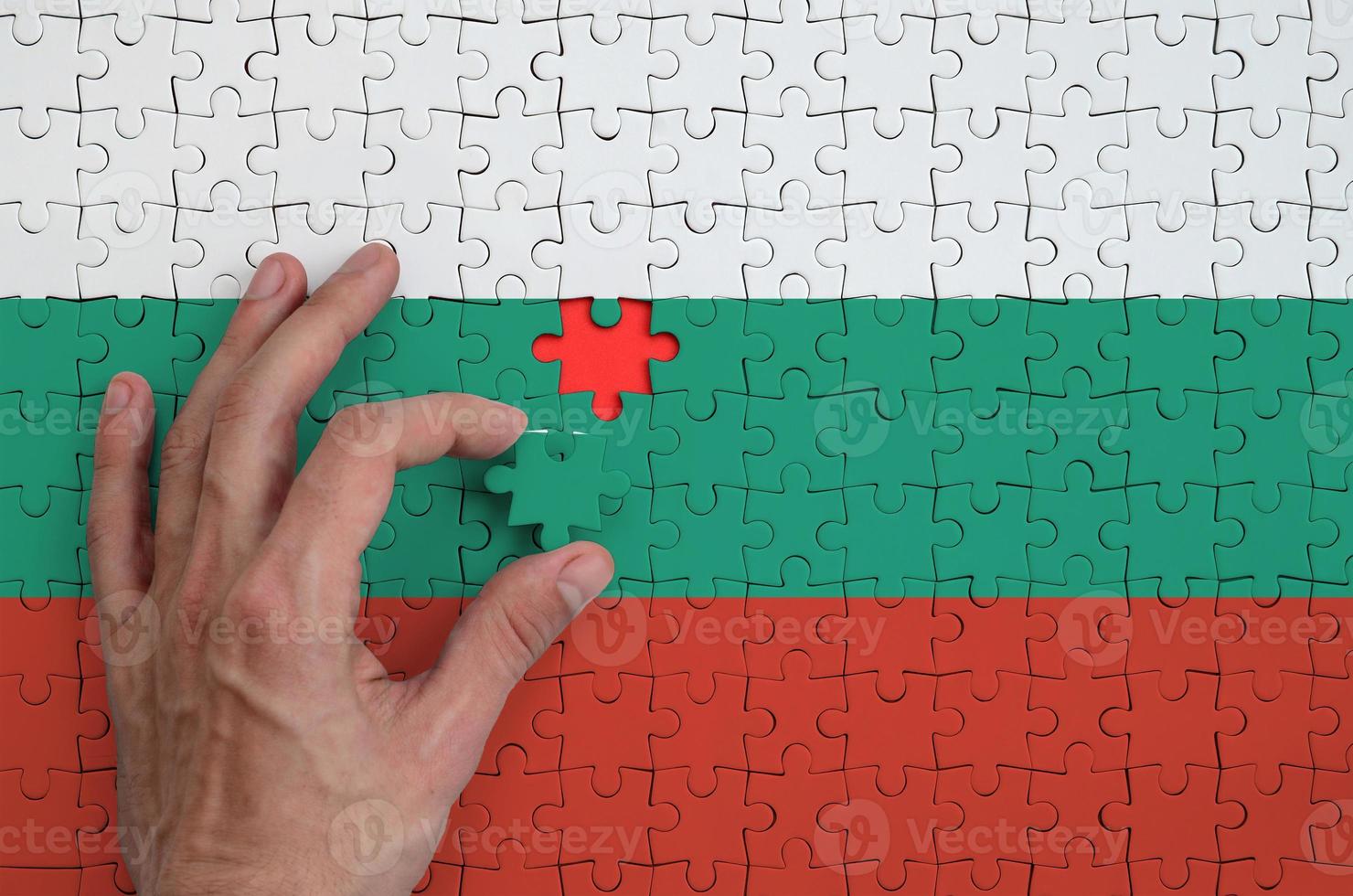 la bandera de bulgaria está representada en un rompecabezas, que la mano del hombre completa para doblar foto