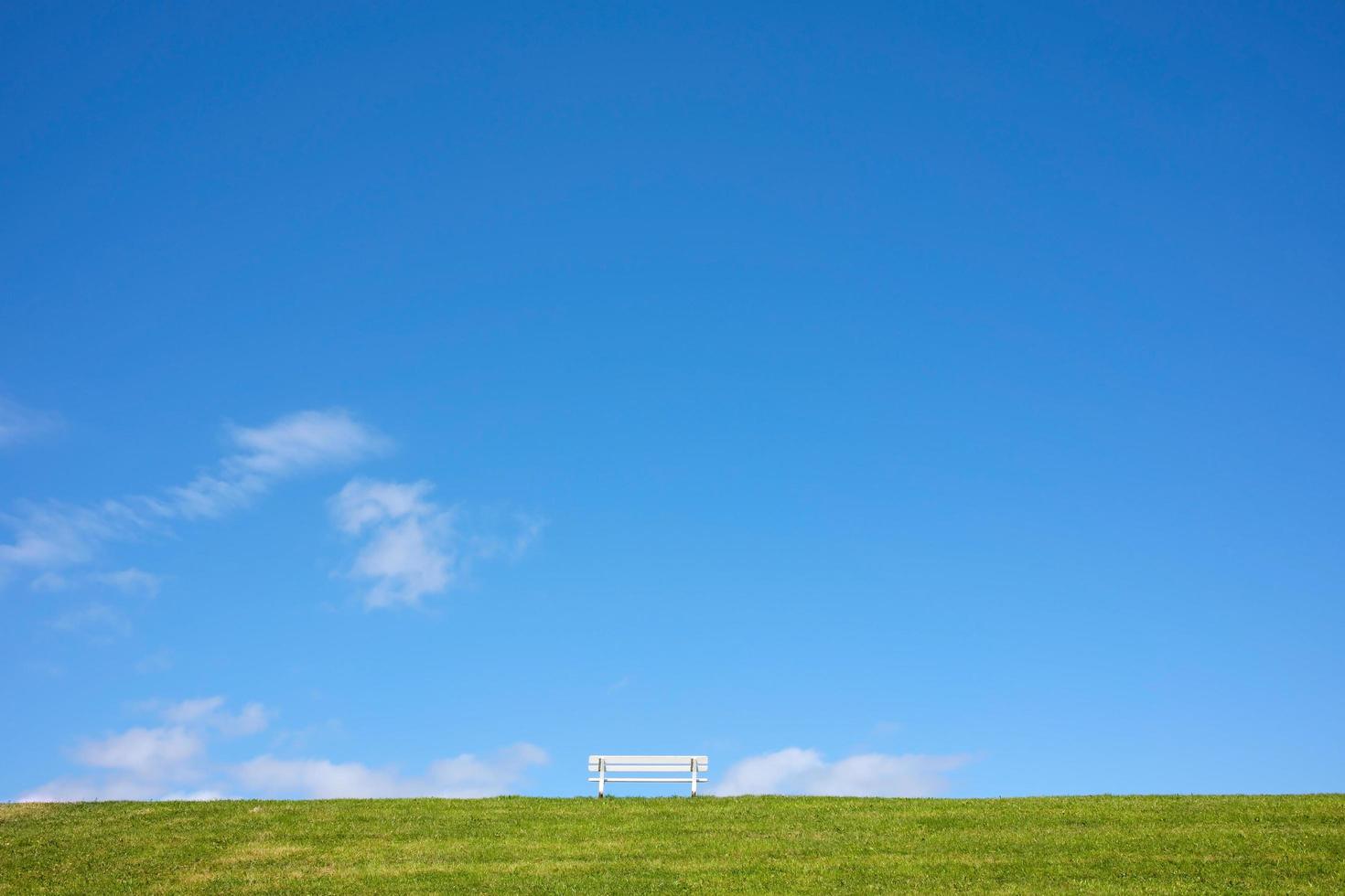 Bench on a green hill, against a background of blue sky and clouds, in a park on a sunny summer day. Beautiful landscape. photo