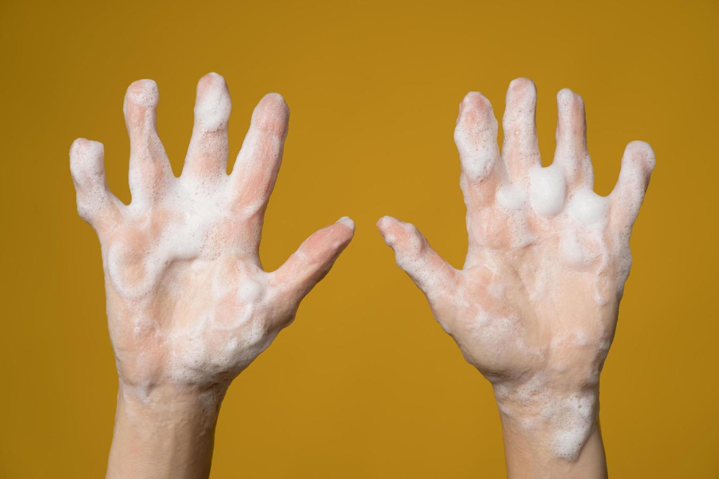 Hands covered with soapy foam. Isolated, on a yellow background. Concept for an effective way to prevent the spread of infections. photo