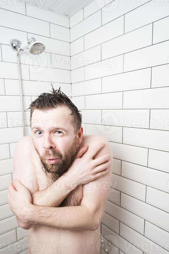 Naked man hugs himself in the shower, he froze and shivers, because suddenly the hot water disappeared and only cold water remained. photo