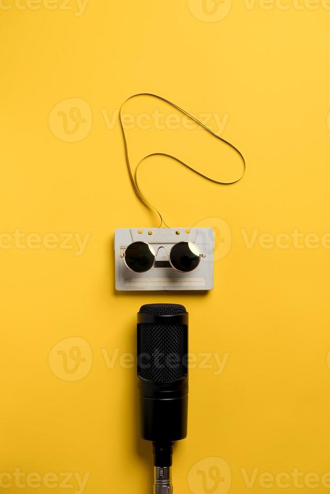 Retro audiotape with magnetic tape in sunglasses and a modern microphone at the bottom. Yellow background. Musical concept. photo