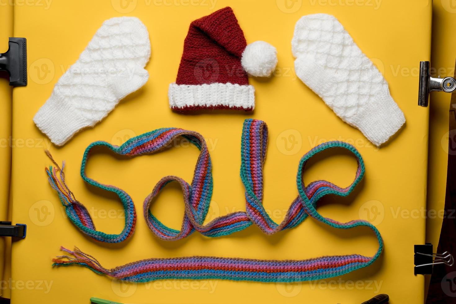 Word SALE is made with a knitted scarf, above it is a Santa Claus hat and mittens. Concept of New Year discounts and shopping. photo