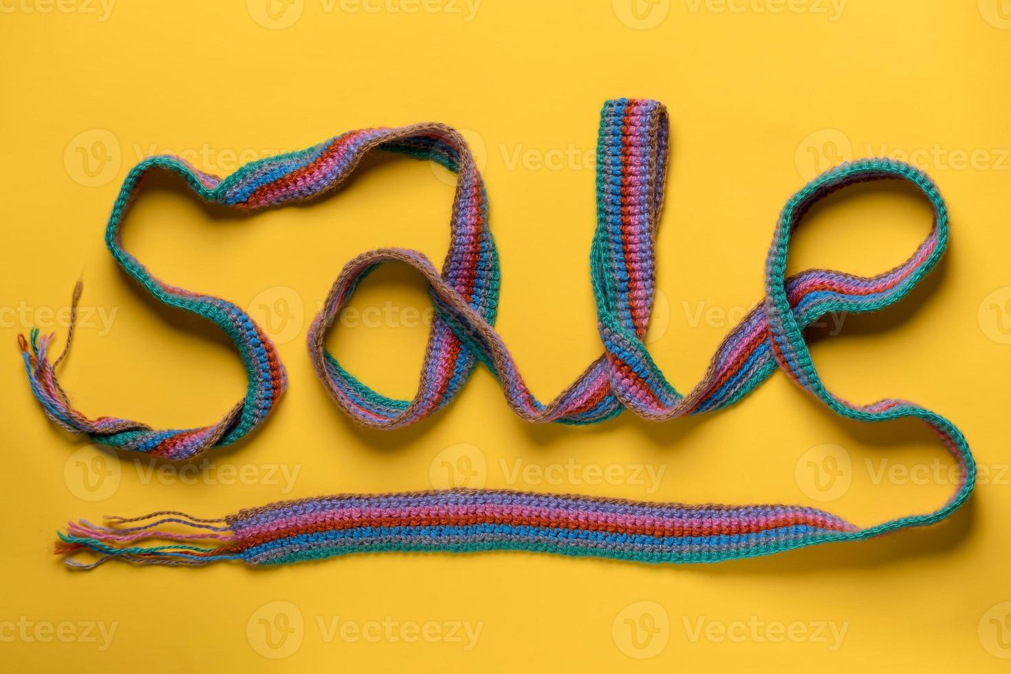 Inscription SALE is made with a multicolored knitted scarf on a yellow background. Concept of New Year's discounts and shopping. photo