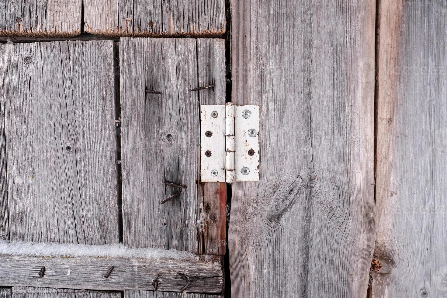 Old hinge on a wooden barn door with rusty nails sticking out of planks in the countryside. Abstract background. photo