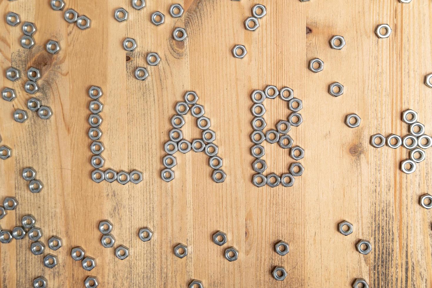 laboratorio de palabras y una flecha que indica la dirección están alineados con tuercas de metal sobre una mesa de madera. Idea creativa. vista superior. foto